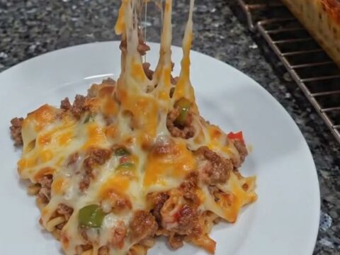 A close-up of a cheesy ground beef and macaroni casserole in a glass dish with a dramatic cheese pull.