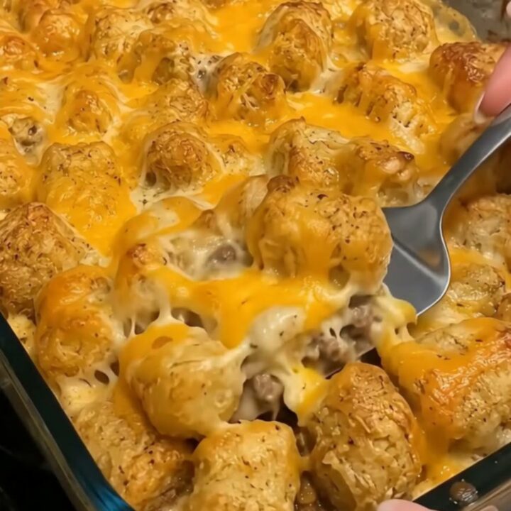A steaming portion of cheesy cowboy casserole with crispy golden tater tots scooped onto a plate.