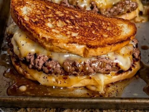 A close-up of a golden-brown patty melt sandwich with cheese stretching from the side.