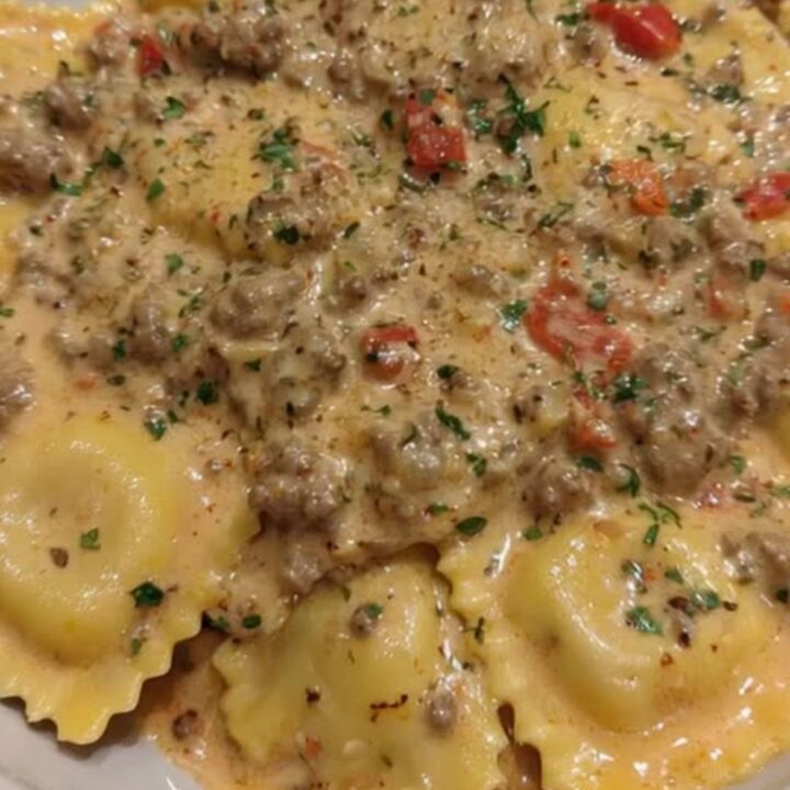 Plated creamy Cajun sausage ravioli smothered in flecked meat sauce and garnished with fresh parsley.