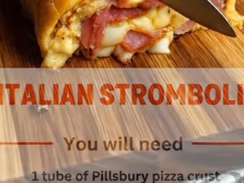 A golden, herb-crusted stromboli on a wooden cutting board, sliced to reveal melted cheese, ham, and salami.