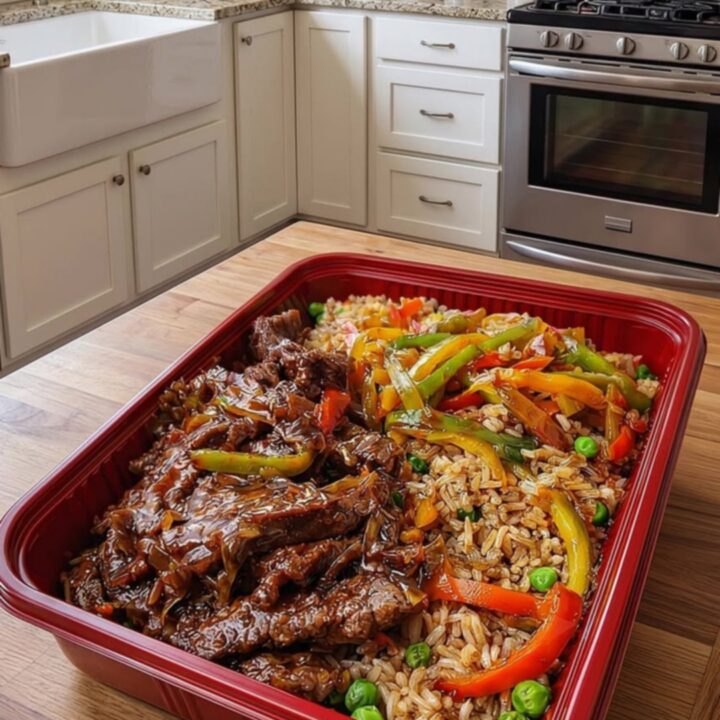 A red rectangular platter featuring glossy pepper steak and colorful vegetable fried rice.