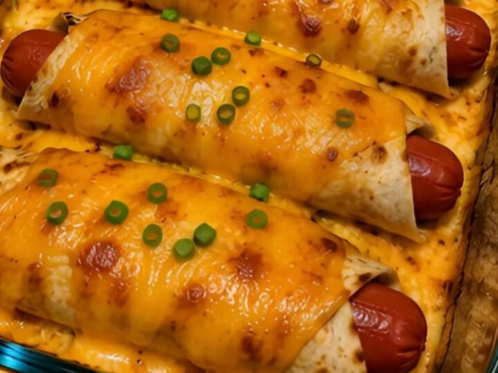 A glass baking dish filled with golden-brown cheesy hot dog wraps topped with fresh green onions.