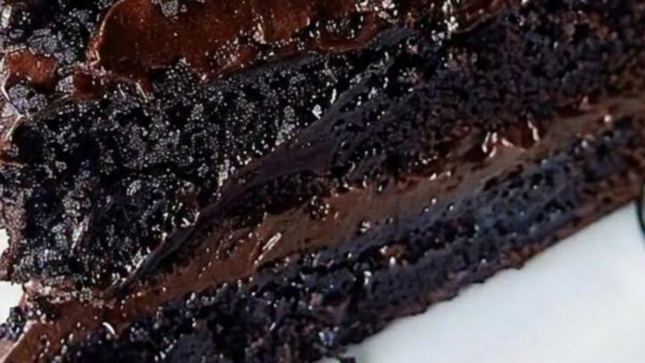 A slice of rich, multi-layered chocolate fudge cake on a white dessert plate with a glossy finish.