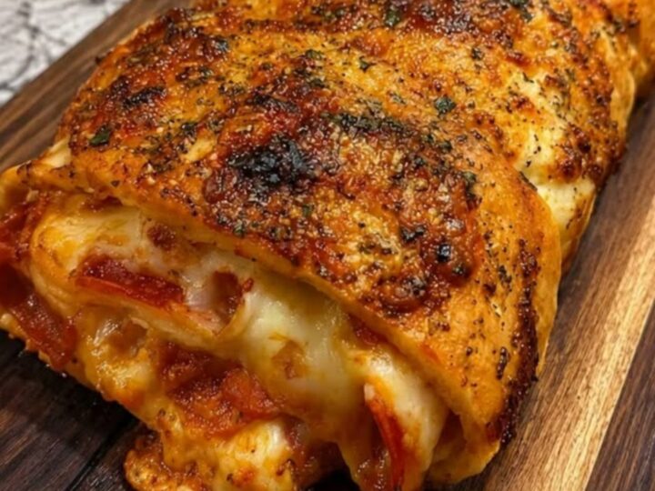 A golden, herb-crusted pepperoni stromboli resting on a wooden board with a slice being lifted to show gooey cheese.