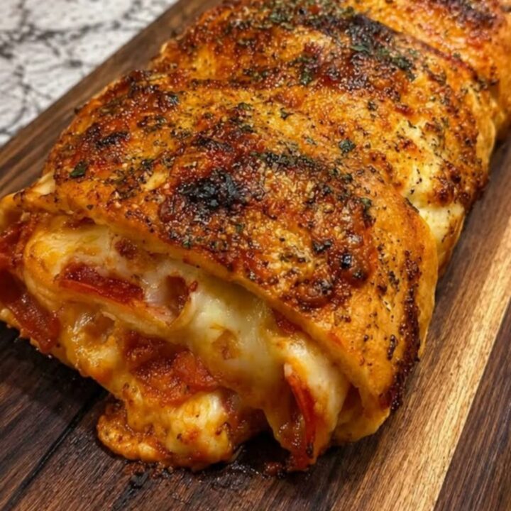 A golden, herb-crusted pepperoni stromboli resting on a wooden board with a slice being lifted to show gooey cheese.