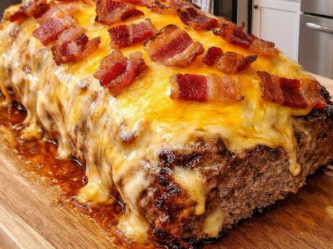 Glazed meatloaf topped with bubbling melted cheese and crispy bacon bits on a wooden board.