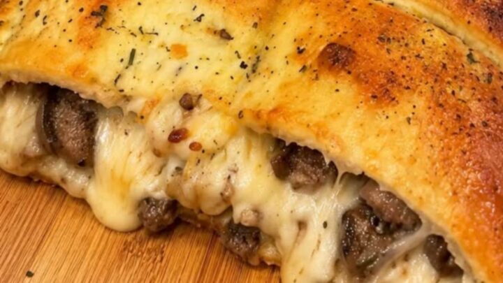 A golden, crusty sausage and mozzarella stuffed bread loaf resting on a rustic wooden cutting board.