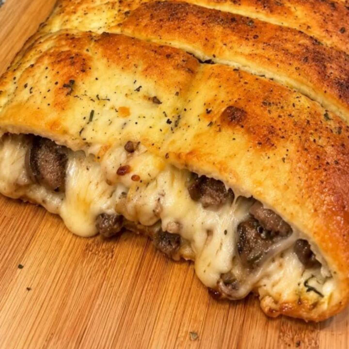 A golden, crusty sausage and mozzarella stuffed bread loaf resting on a rustic wooden cutting board.