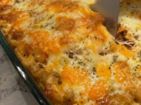 A steaming, golden-brown cheesy beef lasagna in a glass dish with a spatula lifting a portion.