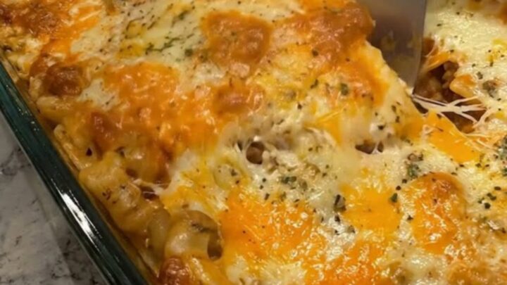 A steaming, golden-brown cheesy beef lasagna in a glass dish with a spatula lifting a portion.