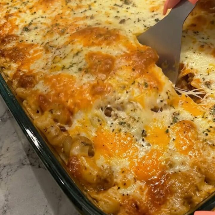 A steaming, golden-brown cheesy beef lasagna in a glass dish with a spatula lifting a portion.