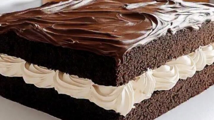 A square slice of chocolate sheet cake with a thick white cream layer and glossy fudge top.