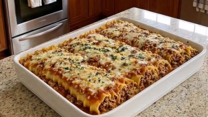 A bubbly, golden-crusted beef lasagna bake in a white ceramic dish sitting on a granite counter.