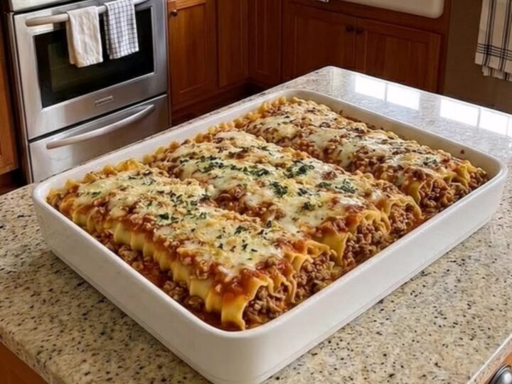 A bubbly, golden-crusted beef lasagna bake in a white ceramic dish sitting on a granite counter.