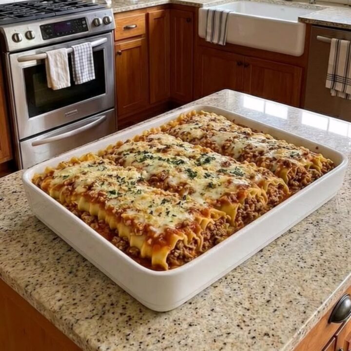 A bubbly, golden-crusted beef lasagna bake in a white ceramic dish sitting on a granite counter.