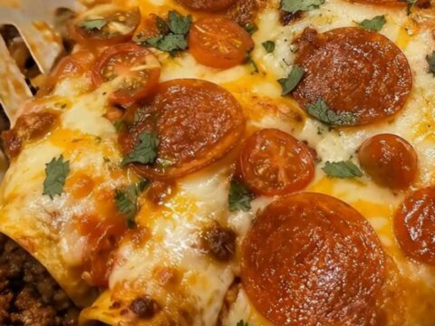 A close up of cheesy pepperoni enchiladas in an oval baking dish, showing melted cheese and crispy pepperoni.