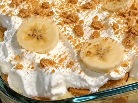 A glass dish filled with layers of vanilla pudding, sliced bananas, and crushed vanilla wafers topped with whipped cream.