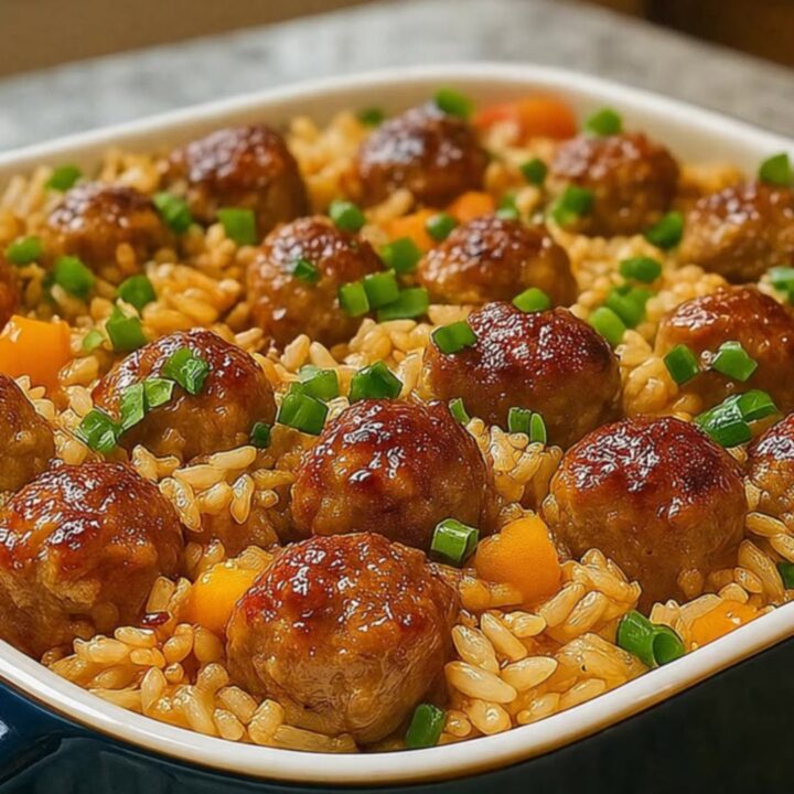 A close-up of a honey garlic meatball rice bake in a glass dish with steam rising.