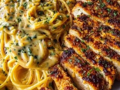 Twirling a fork into creamy garlic parmesan spaghetti with sliced Cajun chicken alongside on a white plate.