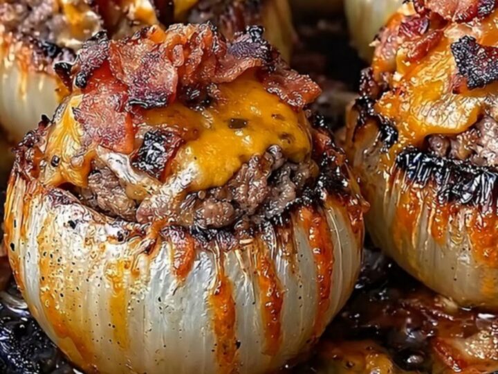 A cast-iron skillet filled with four roasted onion bombs topped with melted, golden cheddar cheese.