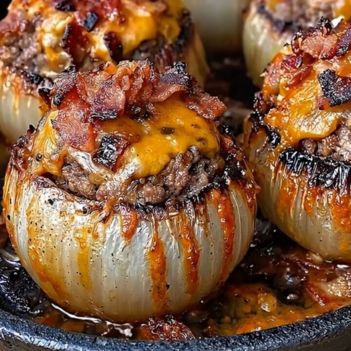 A cast-iron skillet filled with four roasted onion bombs topped with melted, golden cheddar cheese.