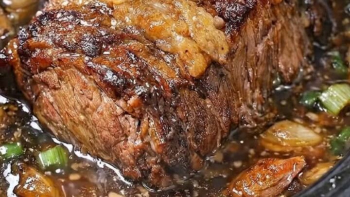 A succulent, tender beef pot roast resting on a white plate with rich garlic broth.