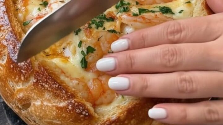 A golden, crusty sourdough bread bowl filled with bubbling melted mozzarella cheese and succulent pink shrimp.