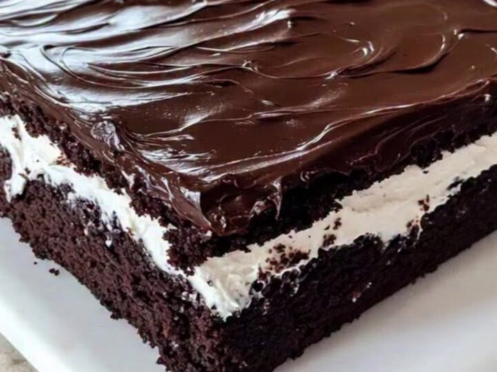 A slice of decadent chocolate sheet cake with a thick white cream filling and a glossy chocolate ganache topping.