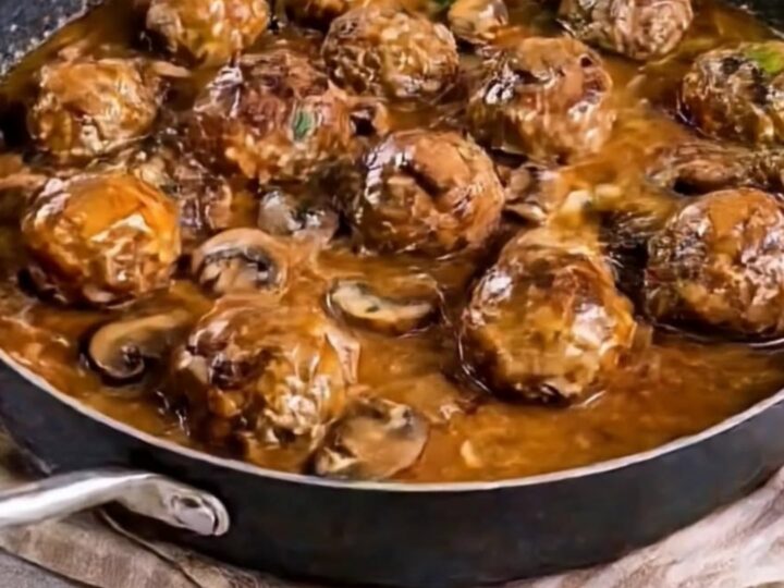 A close-up of tender, juicy beef meatballs in a rich, glossy mushroom gravy served in a large skillet.