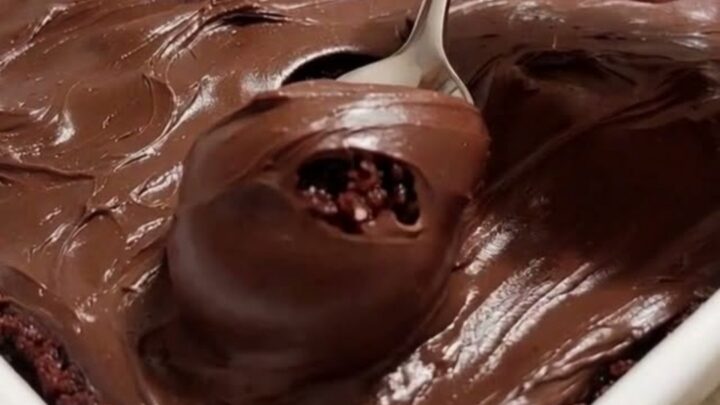 A slice of moist, dark chocolate cake topped with thick chocolate fudge frosting on a white plate.