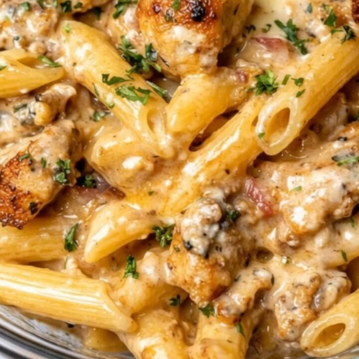 A close-up shot of glossy penne pasta and seared chicken coated in a rich, creamy garlic butter sauce.
