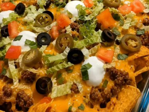 A close-up of a walking taco bake in a glass dish with melted cheese and fresh toppings.