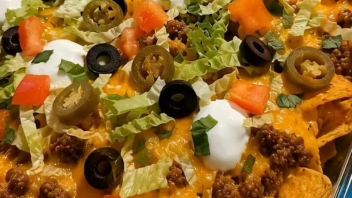 A close-up of a walking taco bake in a glass dish with melted cheese and fresh toppings.
