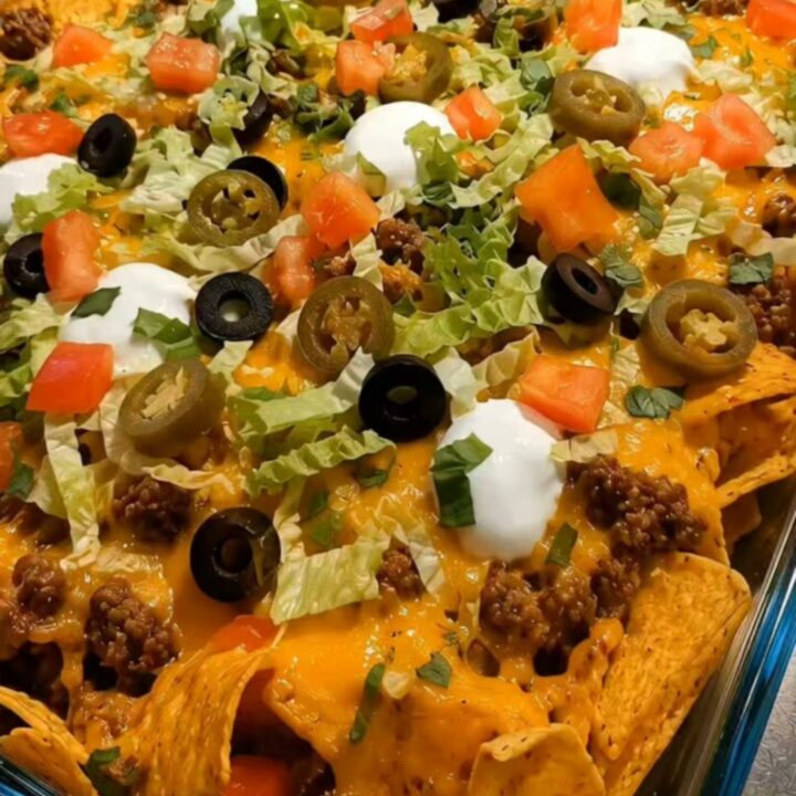 A close-up of a walking taco bake in a glass dish with melted cheese and fresh toppings.