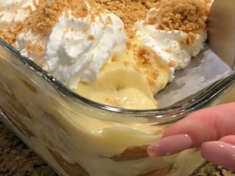 A close-up of a layered banana pudding in a glass dish, showing distinct layers of custard, bananas, and vanilla wafers.