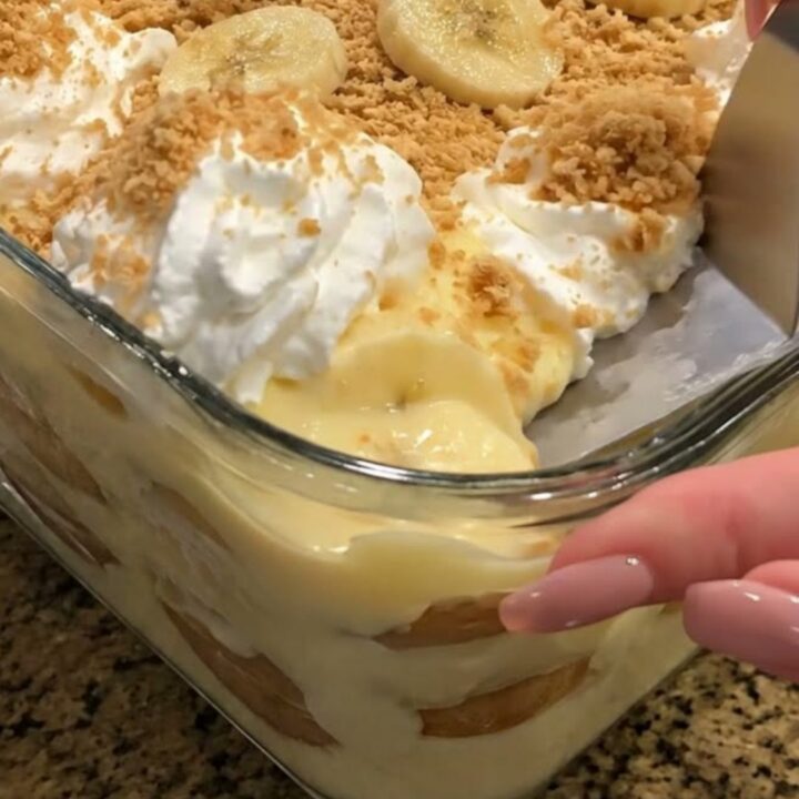 A close-up of a layered banana pudding in a glass dish, showing distinct layers of custard, bananas, and vanilla wafers.