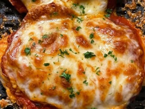 Two golden-brown air-fried chicken breasts topped with melted, bubbling mozzarella cheese and fresh parsley in an air fryer