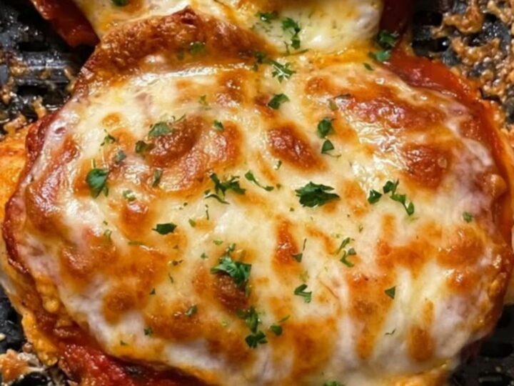 Two golden-brown air-fried chicken breasts topped with melted, bubbling mozzarella cheese and fresh parsley in an air fryer