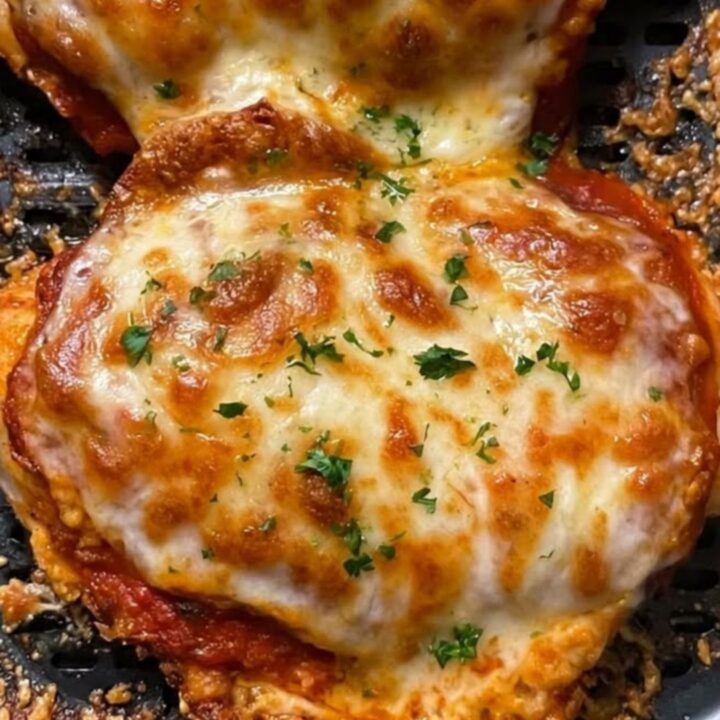 Two golden-brown air-fried chicken breasts topped with melted, bubbling mozzarella cheese and fresh parsley in an air fryer