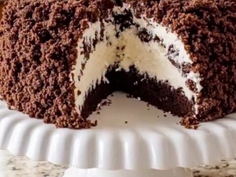 A dome-shaped chocolate crumble cake sits on a white fluted cake stand.