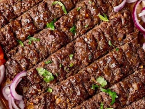 A close-up of juicy, oven-baked kofta kebabs on a baking sheet, garnished with fresh parsley, sliced red onions