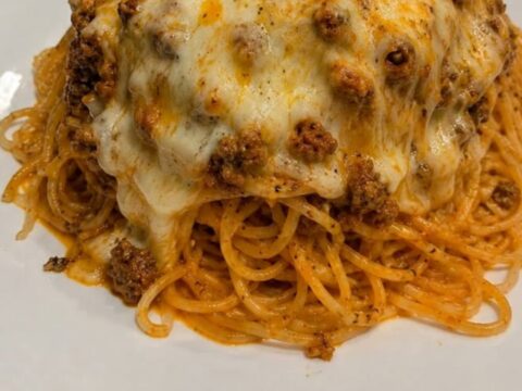 A steaming dish of baked spaghetti with a golden, bubbly cheese crust on a granite counter.
