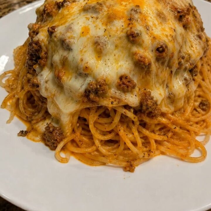 A steaming dish of baked spaghetti with a golden, bubbly cheese crust on a granite counter.