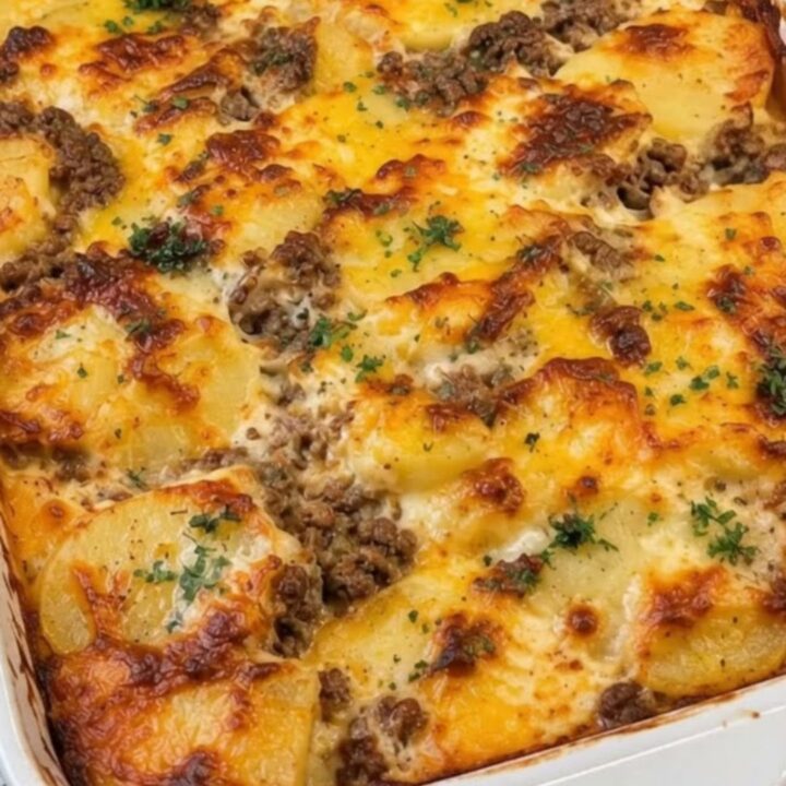 A cheesy cowboy casserole in a white baking dish with melted cheese and tender potato slices.