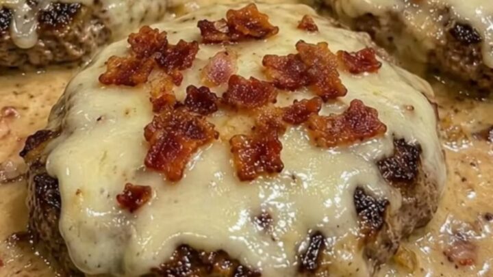 Close-up of a juicy hamburger steak covered in melted Swiss cheese and bacon bits in a creamy sauce.
