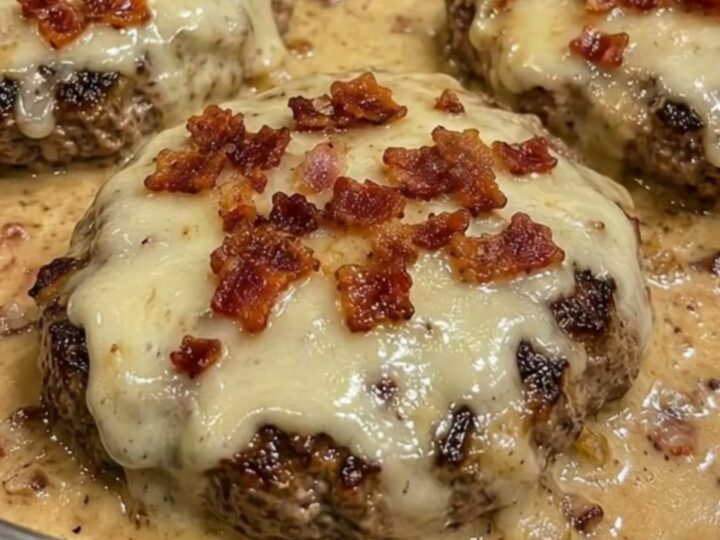 Close-up of a juicy hamburger steak covered in melted Swiss cheese and bacon bits in a creamy sauce.