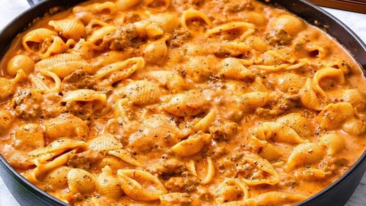 A steaming black skillet filled with creamy beef and shells, showing a delicious cheese pull from a serving spoon.