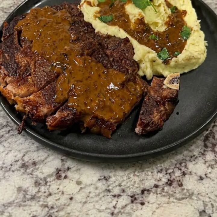A plate featuring seared, sliced steak with rich gravy and creamy mashed potatoes.