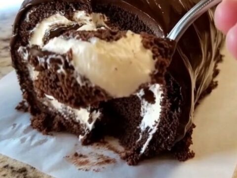 A glossy chocolate-glazed Swiss roll resting on parchment paper with a beautiful spiral visible.